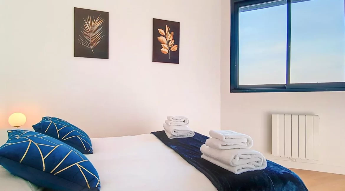 chambre ensoleillee cosy location appartement court sejour argenteuil Chambre lumineuse avec lit et coussins bleus.