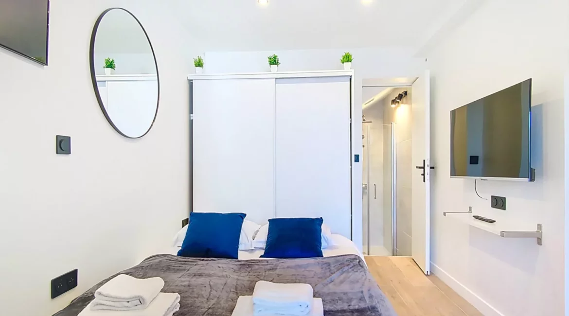 chambre lit tv location appartement argenteuil Chambre moderne avec lit, télévision et miroir.