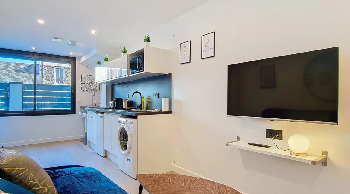 Salon moderne avec cuisine équipée et télévision murale.