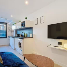 Salon moderne avec cuisine équipée et télévision murale.