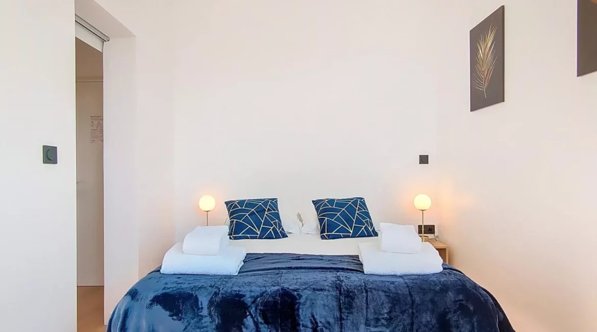 lit double avec decoration murale location appartement court sejour argenteuil Chambre moderne avec lit, décor bleu.