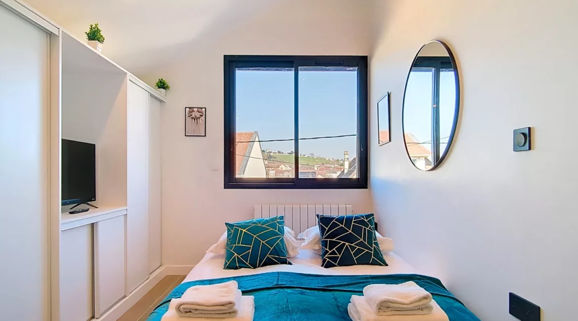 Chambre lumineuse avec lit, fenêtre et miroir rond.