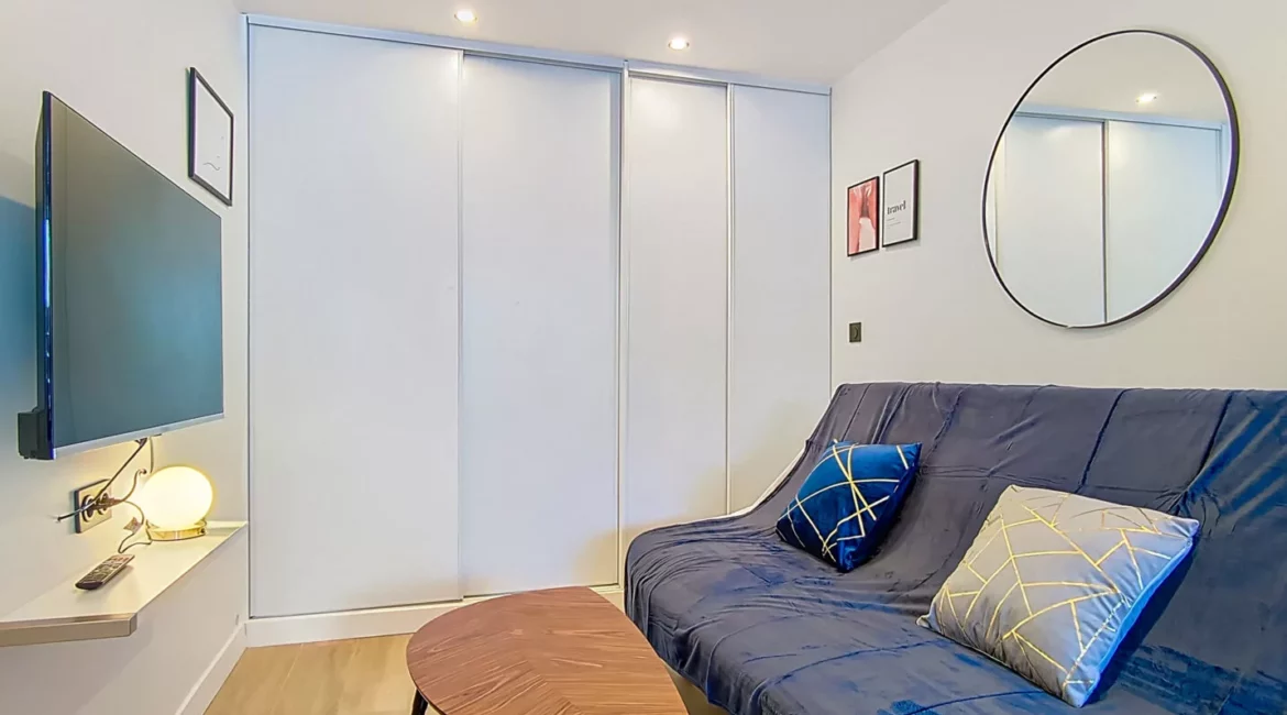 Salon moderne avec canapé bleu et télévision.