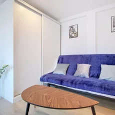 canapé location studio voyage argenteuil Salon moderne avec canapé bleu et table en bois.