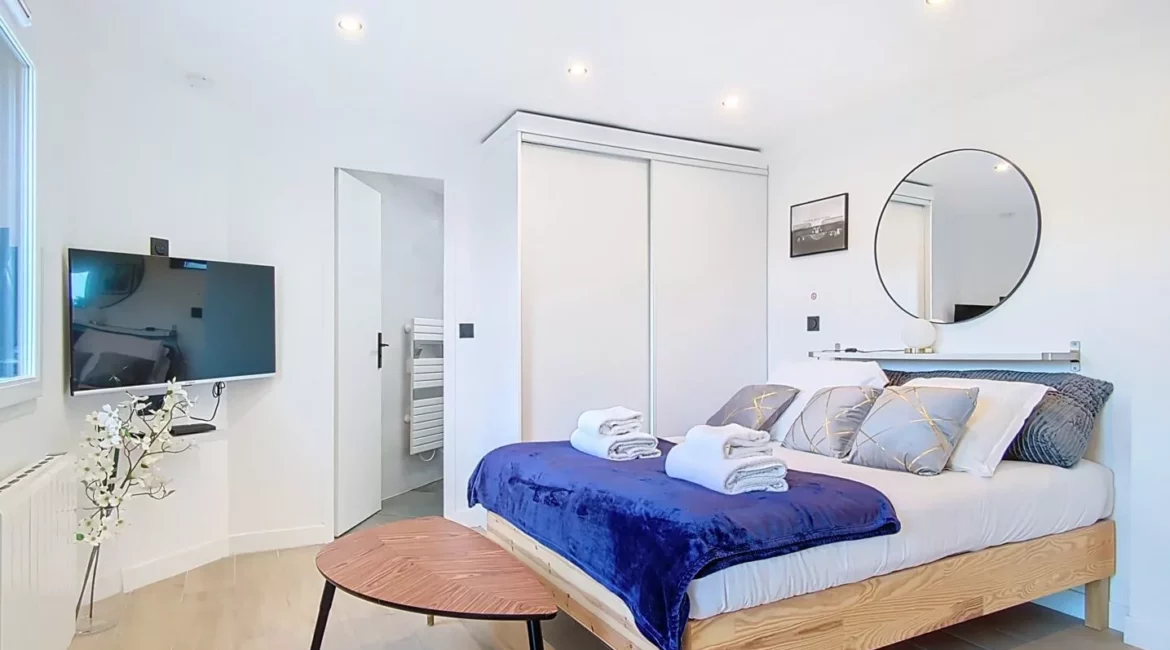 Chambre moderne avec lit double, TV et miroir.